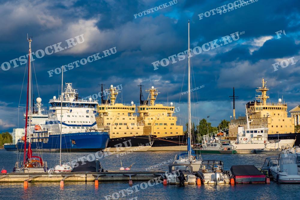 Фотография круизных лайнеров и яхт, пришвартованных в порту, на фоне тёмного и облачного неба.